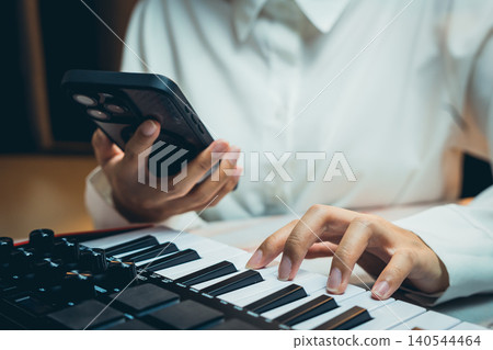Pianist Concept. Musician with Smartphone Creates Melodies on Keyboard in Modern Studio Setting Pianist Concept. Musician with Smartphone Creates Melodies on Keyboard in Modern Studio Setting 140544464