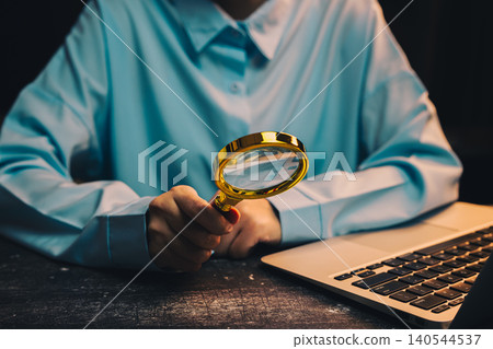 businessman working. Person Holding Magnifying Glass While Working on Laptop in Dark Environment with Blue Shirt 140544537