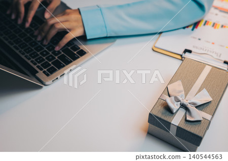 Gift concept. Hands Typing on Laptop Near Gift Box on White Desk with Colorful Charts and Documents 140544563