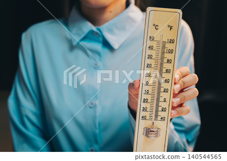 Thermometer concept. Woman in Blue Shirt Holding Wooden Thermometer with Temperature Scale in Studio Environment 140544565