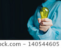 Idea concept. Person Holding Yellow Light Bulb in Blue Shirt Against Dark Background for Creative Ideas and Innovation Concepts 140544605