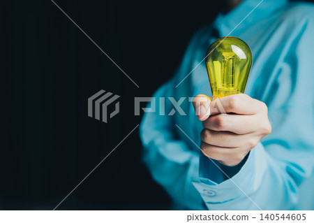 Idea concept. Person Holding Yellow Light Bulb in Blue Shirt Against Dark Background for Creative Ideas and Innovation Concepts 140544605