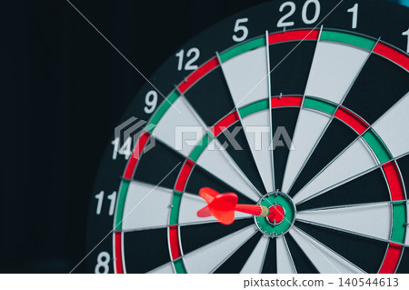 Business Target concept. Focused Dart Hitting Bullseye on Traditional Dartboard with Numbers and Segments in Dark Background Business Target concept. Focused Dart Hitting Bullseye on Traditional Dartboard with Numbers and Segments in Dark Background 140544613