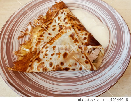 Fried Crepes with Meat Filling and Sour Cream on a Striped Plate Savory Pancakes Close-up Fried Crepes with Meat Filling and Sour Cream on a Striped Plate Savory Pancakes Close-up 140544648