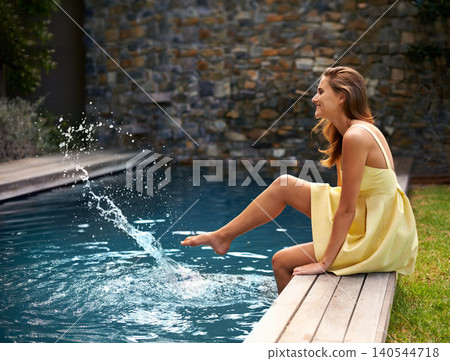Happy, woman and relax with splash in pool on summer, holiday or vacation in California. Girl, smile and sitting outdoor on deck in backyard or garden with feet in water with casual style or fashion Happy, woman and relax with splash in pool on summer, holiday or vacation in California. Girl, smile and sitting outdoor on deck in backyard or garden with feet in water with casual style or fashion 140544718