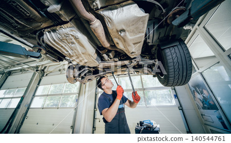Car mechanic examining car suspension of lifted automobile at repair service station Car mechanic examining car suspension of lifted automobile at repair service station 140544761