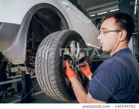 Car mechanic inspecting wheel and suspension detail of lifted automobile at repair service station Car mechanic inspecting wheel and suspension detail of lifted automobile at repair service station 140544762