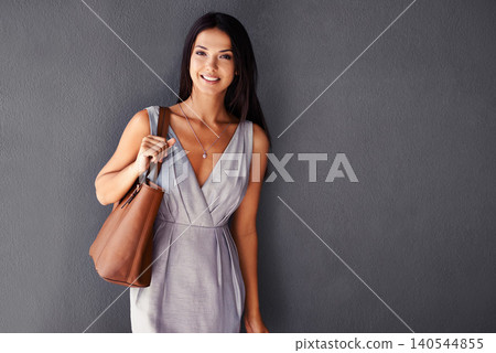 Studio, portrait and purse with fashion, smile and accessories with dress and joy. Woman, face and model with confidence, beauty and happiness with handbag and style isolated on gray wall background Studio, portrait and purse with fashion, smile and accessories with dress and joy. Woman, face and model with confidence, beauty and happiness with handbag and style isolated on gray wall background 140544855