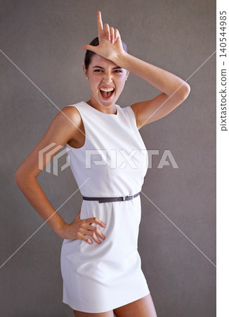 Woman, portrait and hand for letter L in studio, loser and playful body language on gray background. Female person, humor and funny expression for communication, sign and emoji or symbol for mocking Woman, portrait and hand for letter L in studio, loser and playful body language on gray background. Female person, humor and funny expression for communication, sign and emoji or symbol for mocking 140544985