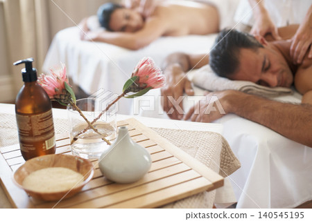 Hotel, flowers and couple in spa to relax on bed or break with luxury pamper treatment tools on table. Protea, facial oil or woman with man at resort or salon for natural healing benefits or massage 140545195