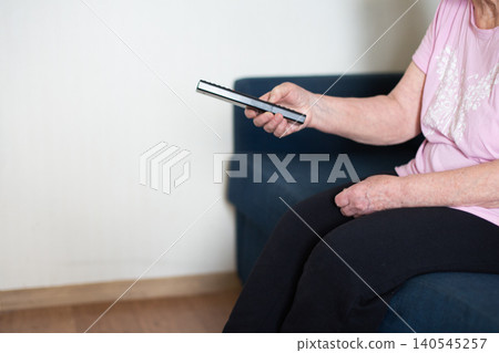 Senior woman holding remote control watching tv at home 140545257
