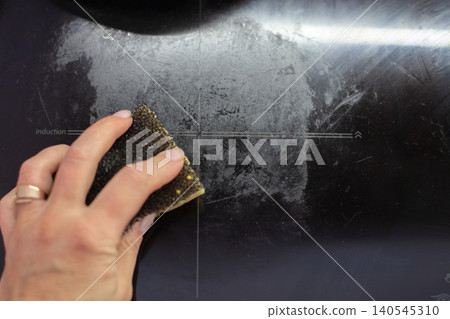 Hand cleaning dirty induction stove top with sponge Hand cleaning dirty induction stove top with sponge 140545310
