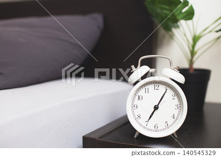 White alarm clock standing on bedside table White alarm clock standing on bedside table 140545329