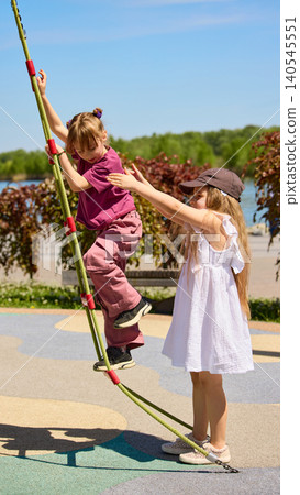 Girl helping younger child climb rope on sunny playground. Girl helping younger child climb rope on sunny playground. 140545551