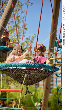 Girls giving high five on playground nest swing in sunny park. Girls giving high five on playground nest swing in sunny park. 140545558