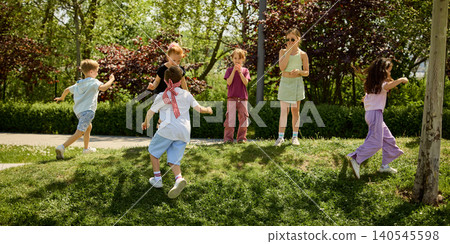 Children running and playing blindfold chase game in green park on sunny day. 140545598
