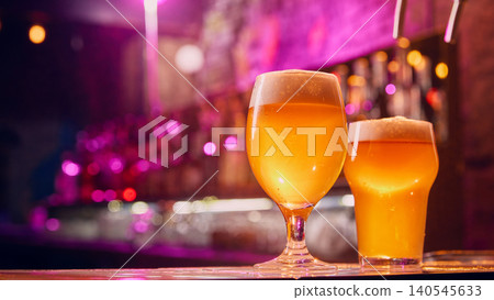 Two craft beer glasses glowing on bar counter with neon bokeh. Two craft beer glasses glowing on bar counter with neon bokeh. 140545633