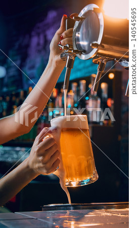 Female hand pouring draft beer into glass mug with overflowing foam. 140545695