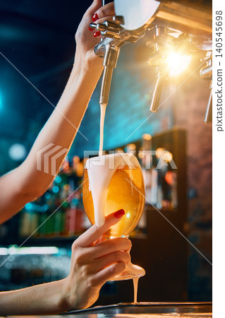 Female bartender filling golden beer glass with creamy foam Female bartender filling golden beer glass with creamy foam 140545698