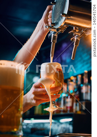 Female bartender pouring draft beer into tulip glass with overflowing foam. Female bartender pouring draft beer into tulip glass with overflowing foam. 140545704