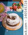 Bulgarian bundt cake with powdered sugar stands on wooden board with rose petals at Rose Festival in Kazanluk. Bread food display shows homemade baking, dessert tradition, festival food, local cuisine 140545728