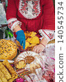 Woman in embroidered dress cuts traditional bread and cake at Kazanluk Rose Festival in Bulgaria. Festival food display features kozunak, banitsa, baking, heritage, community, Bulgarian cuisine 140545734