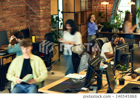 Busy creative office with employees working and moving between desks with motion blur. 140545868