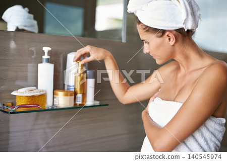 Woman, towel and cosmetics in bathroom with mirror for skincare, beauty and cosmetology for hygiene, fresh and pamper indoor. Young person and touch bottle for groom, spa and care for body and clean Woman, towel and cosmetics in bathroom with mirror for skincare, beauty and cosmetology for hygiene, fresh and pamper indoor. Young person and touch bottle for groom, spa and care for body and clean 140545974
