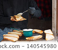 Cook spreading savory topping on grilled sourdough street food at Naplavka market 140545980