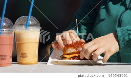 Hands holding gourmet burger with fruit smoothies at food festival in Karlin 140545991