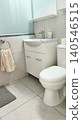 Vertical view of a modern clean bathroom featuring a toilet, sink vanity, soft towel, and tiled walls. Bright minimalist interior with a fresh, hygienic, and comfortable atmosphere. 140546515