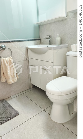 Vertical view of a modern clean bathroom featuring a toilet, sink vanity, soft towel, and tiled walls. Bright minimalist interior with a fresh, hygienic, and comfortable atmosphere. Vertical view of a modern clean bathroom featuring a toilet, sink vanity, soft towel, and tiled walls. Bright minimalist interior with a fresh, hygienic, and comfortable atmosphere. 140546515