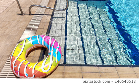 Colorful inflatable donut float beside a sparkling swimming pool on a sunny day, symbolizing summer vacation, relaxation, leisure, and fun outdoor recreation Colorful inflatable donut float beside a sparkling swimming pool on a sunny day, symbolizing summer vacation, relaxation, leisure, and fun outdoor recreation 140546518
