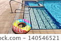 inflatable donut ring float with pink frosting print and multicolor sprinkle pattern on pool deck beside hotel pool, full donut resting on tiled poolside in summer 140546521