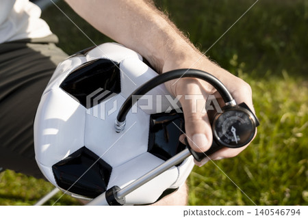 Man inflates a soccer ball with a hand pump featuring a pressure gauge, capturing the simple routine of grassroots football. Man inflates a soccer ball with a hand pump featuring a pressure gauge, capturing the simple routine of grassroots football. 140546794