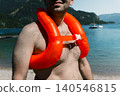 Man wearing an orange inflatable life vest standing on a lake shore, capturing a mountain lake lifestyle and relaxed summer vibes 140546815