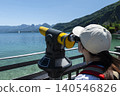 Woman looking through a coin operated telescope at mountains and lake Wolfgangsee in Austria, emphasizing outdoor observation 140546826