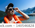 Man wearing an orange inflatable life vest standing on a lake shore, capturing a mountain lake lifestyle and relaxed summer vibes 140546828