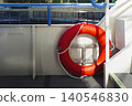 Bright orange lifebuoy on a boat deck with blue railings, representing water transport and the boating environment 140546830