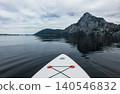 First person view from a white stand up paddleboard on calm lake Traunsee in the Austrian Alps, capturing summer water activity. 140546832