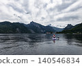 Paddleboarder moving on lake Traunsee with mountains and a lakeside settlement in the background, capturing a exploration moment. 140546834