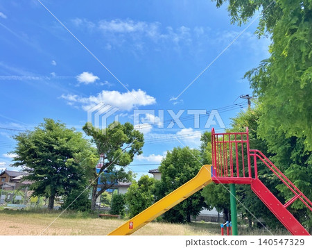 Blue sky and a park slide: a peaceful scene in a residential area. Blue sky and a park slide: a peaceful scene in a residential area. 140547329