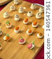 Gourmet canapes appetizer served on wooden board with sauces, sprouts, cheese, sesame. Small bites with toasted bread, microgreens, various savory toppings for guests, serving dishes at event 140547361