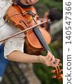 Violin woman player performs live music outdoors, with violin and bow captured close up, cultural performance. Classical music, city live music, musician hands, string instrument, event promotion 140547366