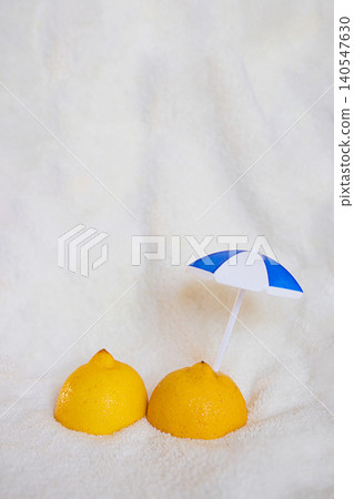 Two yellow lemons with a small blue and white beach umbrella placed on a soft white surface, creating a playful summer-themed composition Two yellow lemons with a small blue and white beach umbrella placed on a soft white surface, creating a playful summer-themed composition 140547630