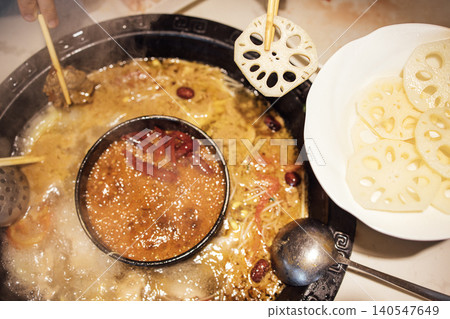 Hot pot meal featuring a bubbling broth with various ingredients, including lotus root slices and chopsticks, served in a traditional round pot on a dining table Hot pot meal featuring a bubbling broth with various ingredients, including lotus root slices and chopsticks, served in a traditional round pot on a dining table 140547649