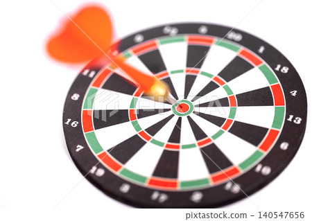 Dart with orange flight embedded in the bullseye of a black and white dartboard, featuring red and green segments, isolated on a white background Dart with orange flight embedded in the bullseye of a black and white dartboard, featuring red and green segments, isolated on a white background 140547656