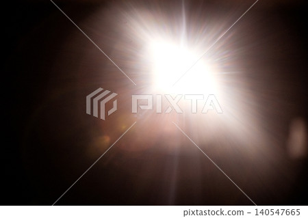 Bright light source emitting rays and flares against a dark background, creating a dramatic illumination effect with visible light distortion and reflections Bright light source emitting rays and flares against a dark background, creating a dramatic illumination effect with visible light distortion and reflections 140547665