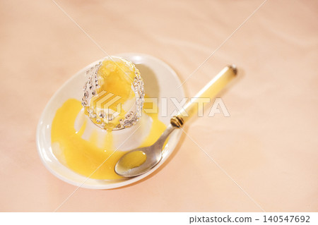 Egg dessert with silver foil on a white plate, yellow sauce drizzled around, accompanied by a silver spoon on a soft pastel background Egg dessert with silver foil on a white plate, yellow sauce drizzled around, accompanied by a silver spoon on a soft pastel background 140547692