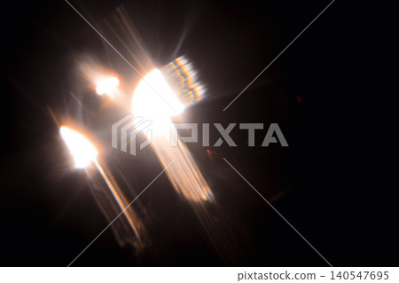 Bright car headlights shining through darkness, creating a dramatic light effect with lens flare and reflections visible in a black background Bright car headlights shining through darkness, creating a dramatic light effect with lens flare and reflections visible in a black background 140547695